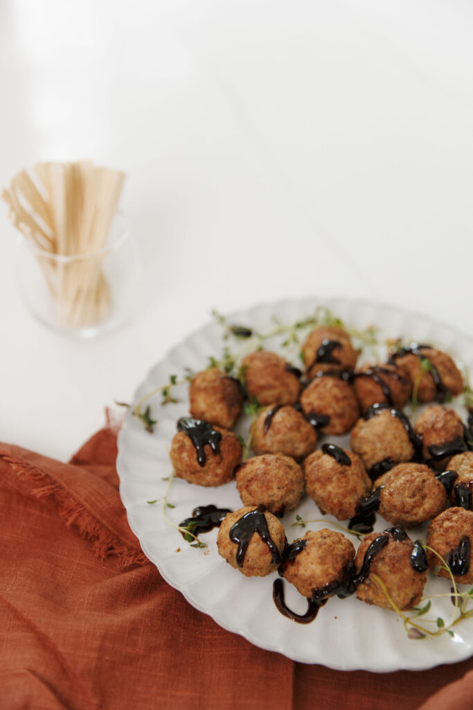 Glazed meatballs on serving platter with cocktail picks and herbs.